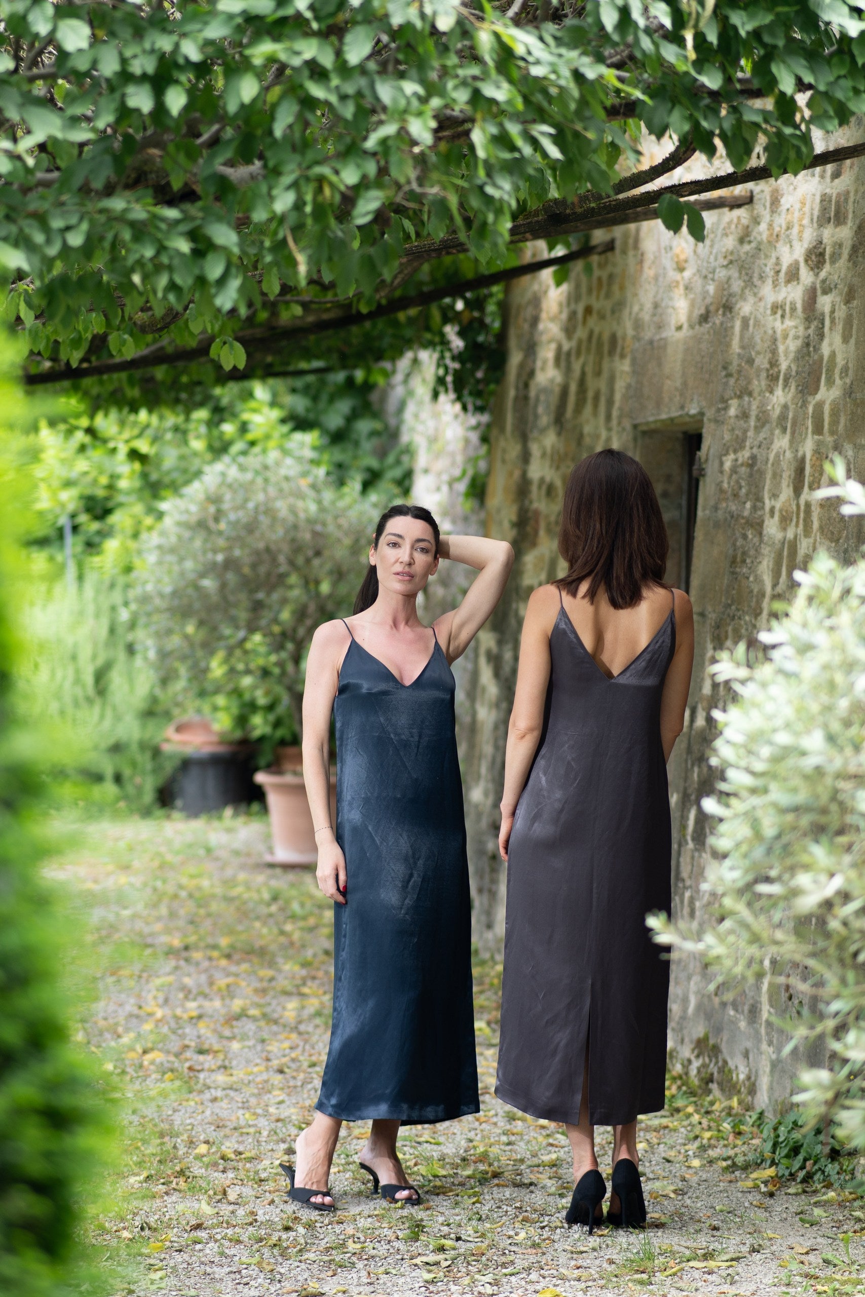 Two women wearing dark blue slip dresses standing in a garden.