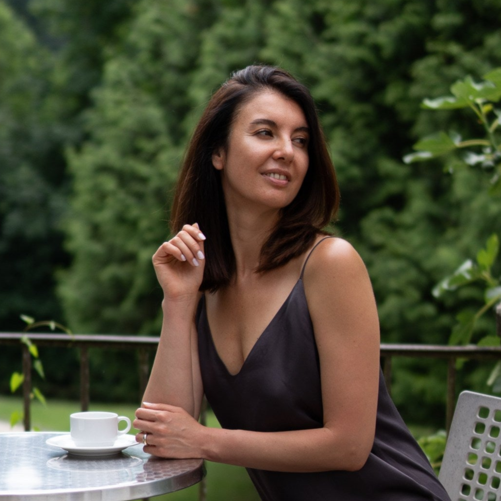 Woman sitting at a table outdoors with a blurred green background