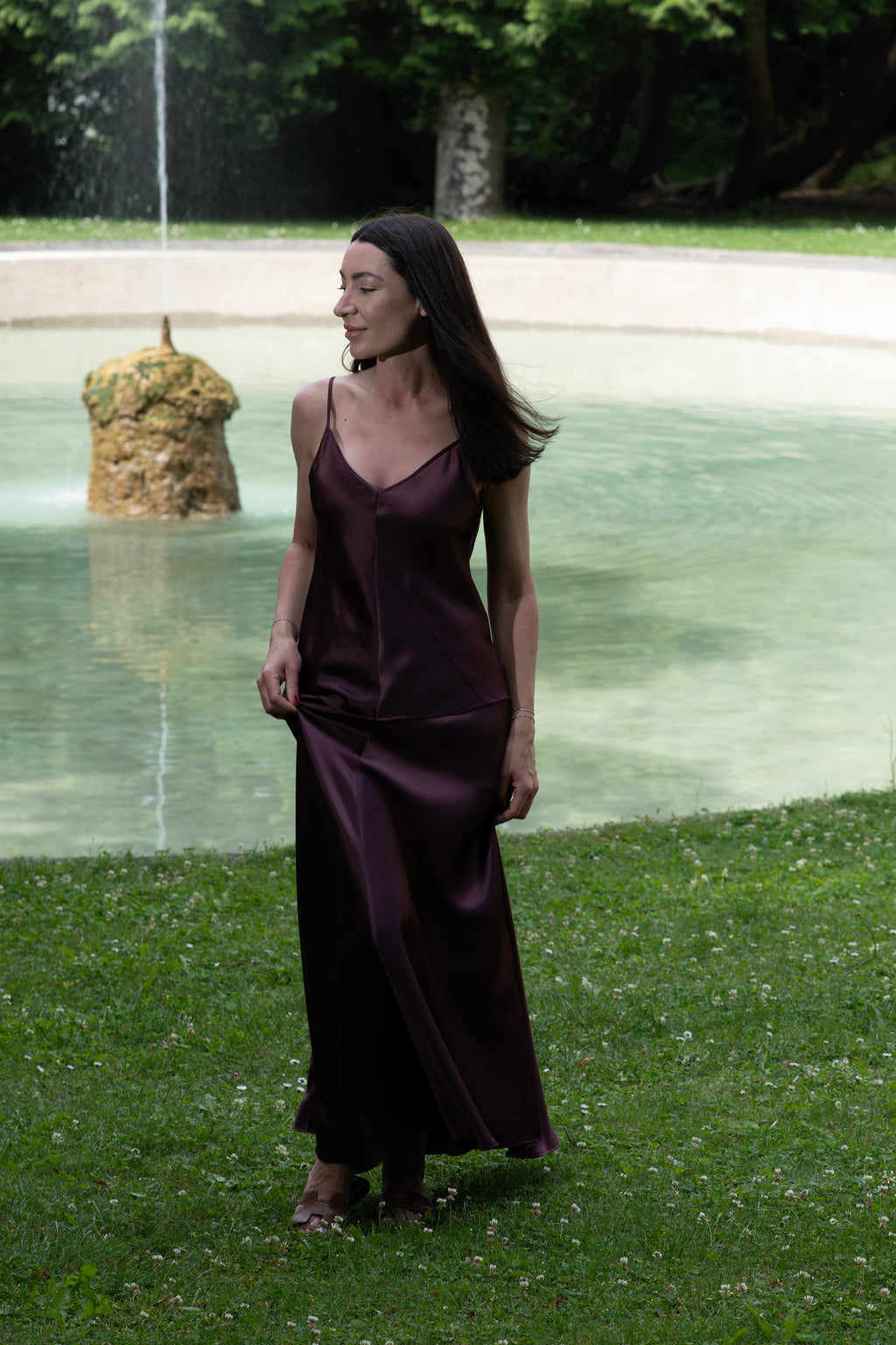Woman in a purple dress standing by a fountain in a park