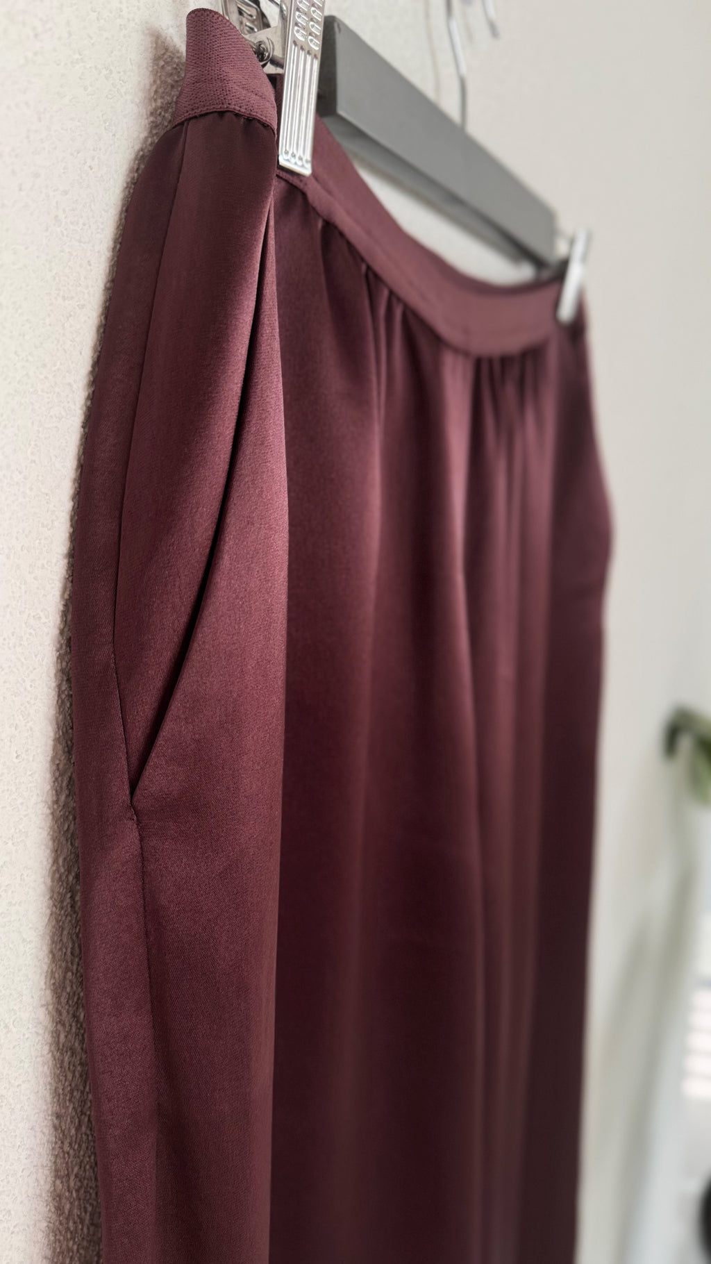 Maroon trousers hanging on a hanger against a neutral wall.